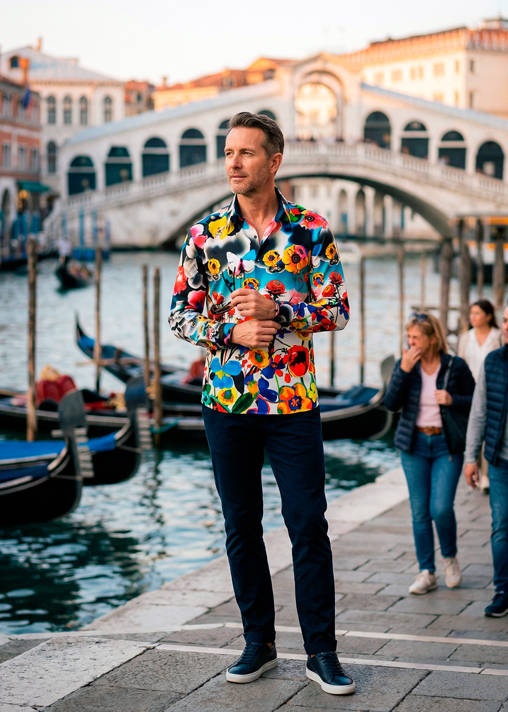 A man stands on the Grand Canal in Venice in front of the Rialto Bridge wearing the colorful FLOWERDREAM shirt by GERMENS artfashion.