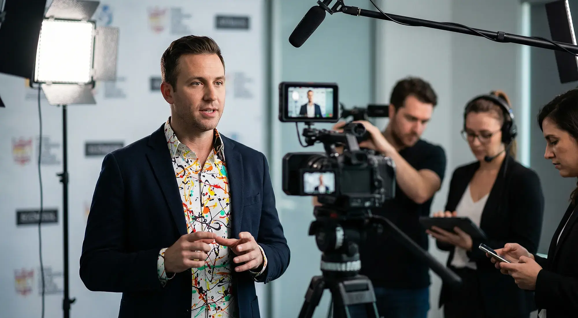 Recording for a social media post. The speaker is wearing a suit with the GERMENS FRISKY shirt underneath.