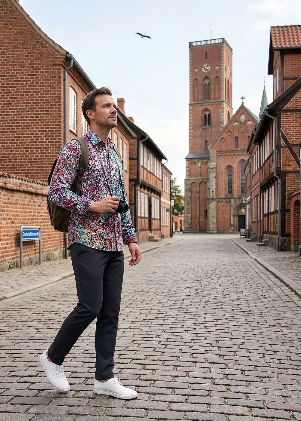 A tourist strolls through the city center of Ribe in Denmark. He is wearing the colorful FRAXI MULTISE shirt from GERMENS.