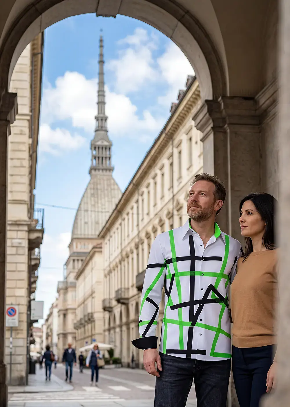 A married couple visits the Italian city of Turin during their summer vacation. The man wears the white, green, and black TIOLI shirt from GERMENS.
