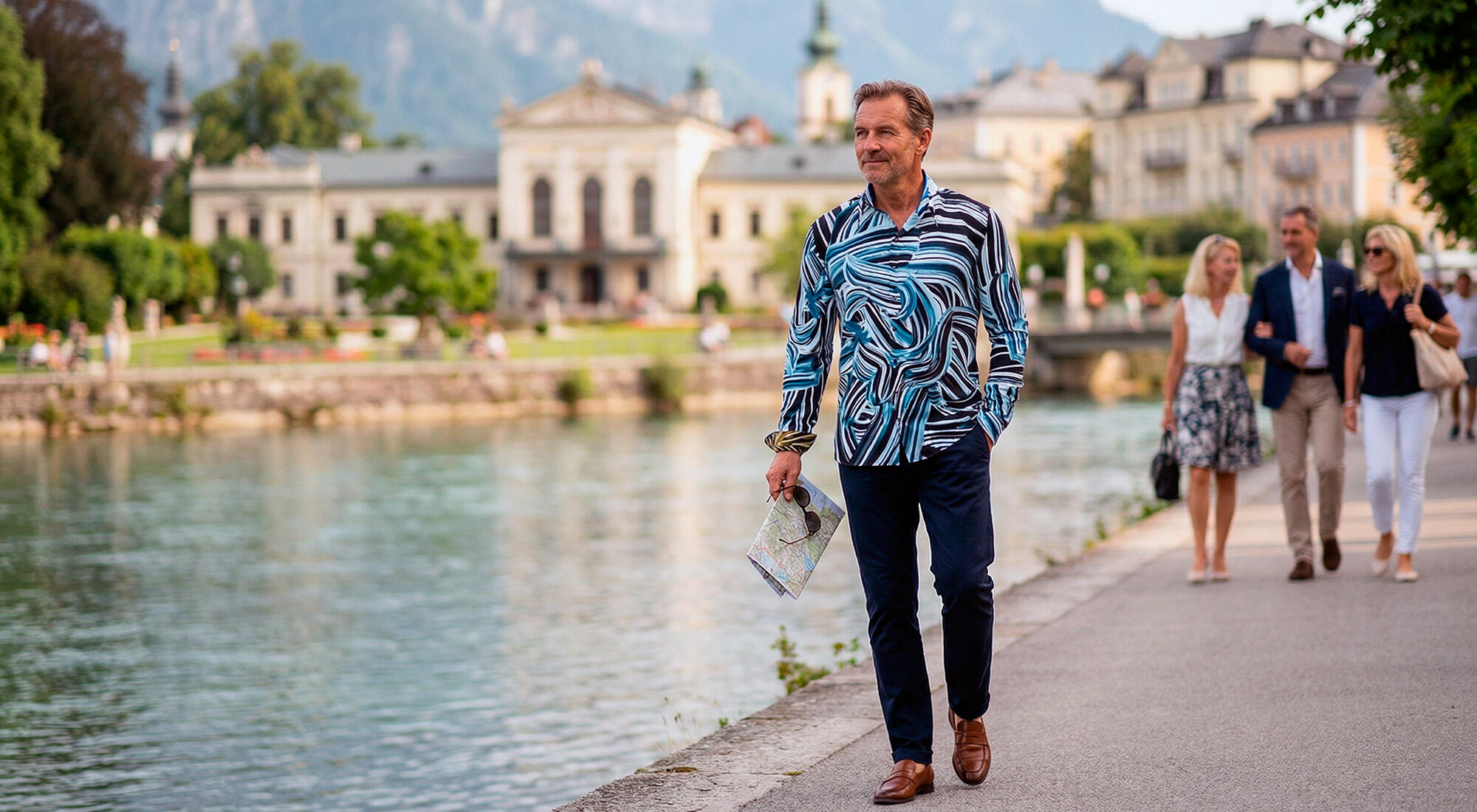 A man is walking along the waterfront in Bad Ischl. He is wearing the black and blue BRUSHSTROKE shirt by GERMENS.