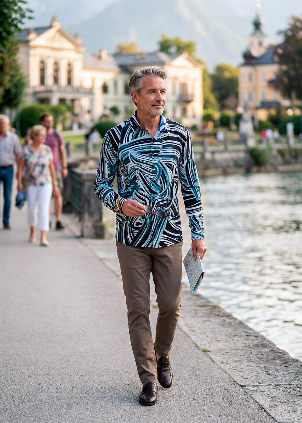 A man is walking along the waterfront in Bad Ischl. He is wearing the black and blue BRUSHSTROKE shirt by GERMENS.
